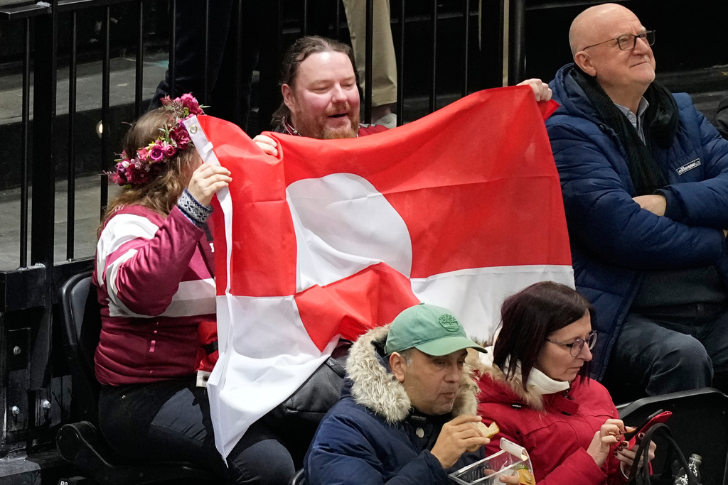 Fans hold Greenland national flag before a preliminary round match of men's ice hockey between United States and Denmark at the 2026 Winter Olympics, in Milan, Italy, Saturday, Feb. 14, 2026. (AP Photo/Hassan Ammar)
