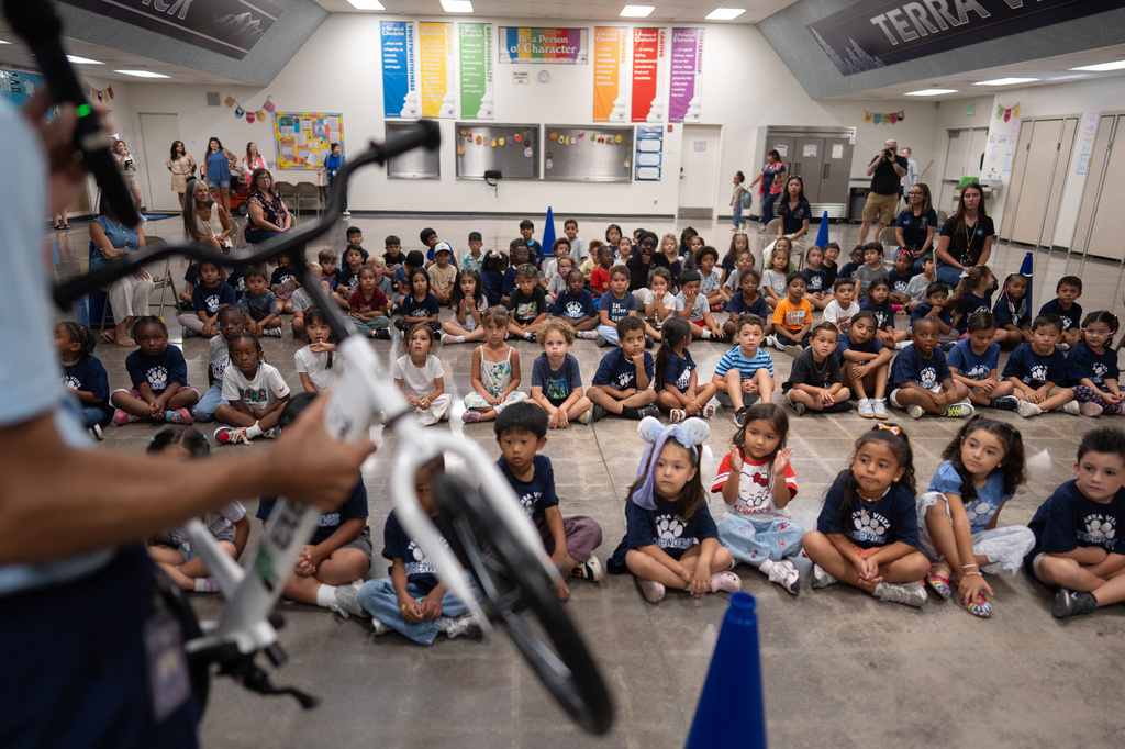 Physical education teacher Ray Herrera demonstrates how to ride a bike as students gather for a learn-to-ride program at Terra Vista Elementary School in Rancho Cucamonga, Calif., Wednesday, Sept. 2, 2026. (AP Photo/Jae C. Hong)