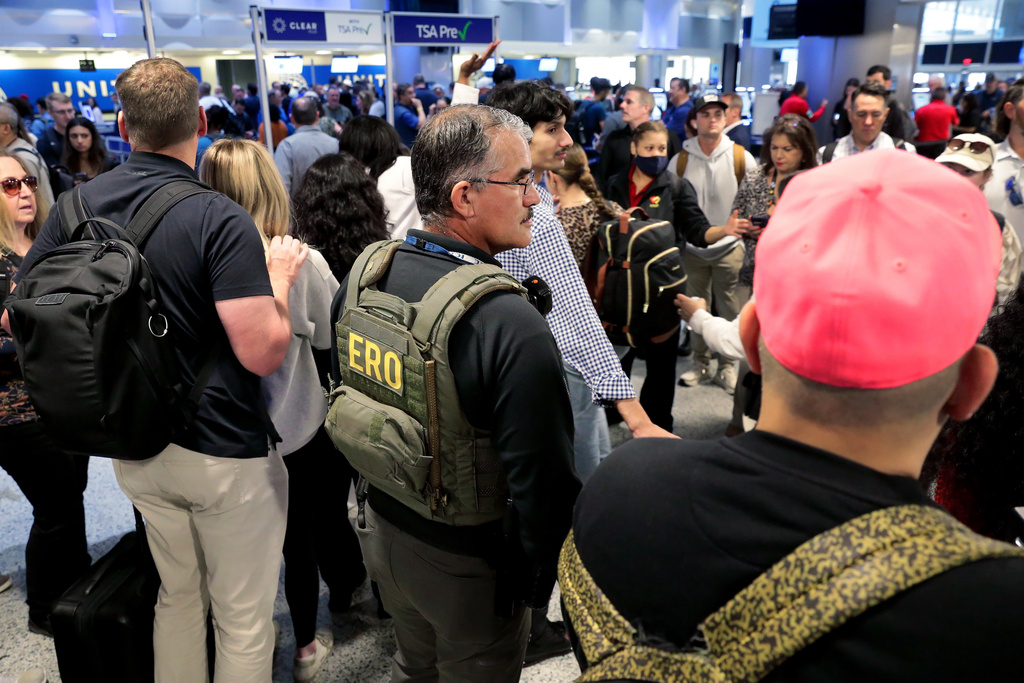 A federal immigration agent stands amid air travelers to assist with security across the lines of people waiting to progress through the TSA checkpoint in Terminal C at the George Bush Intercontinental Airport, Monday, March 23, 2026, in Houston. (AP Photo/Michael Wyke)
