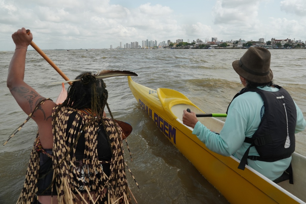 Participants in the People's Summit event paddle on Guajara Bay during the COP30 U.N. Climate Summit, Wednesday, Nov. 12, 2025, with the skyline of Belem, Brazil. (AP Photo/Joshua A. Bickel)