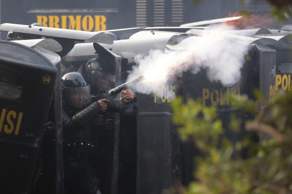 Police officers fire tear during a protest following the death of a delivery rider in clashes between riot police and students protesting against lawmakers' allowances, in Surabaya, East Java, Indonesia, Friday, Aug. 29, 2025. (AP Photo/Trisnadi)