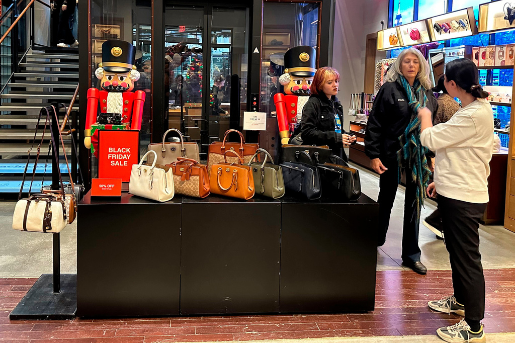 FILE - Shoppers pause near a display of handbags at a Coach store in New York on Sunday, Nov. 19, 2023. (AP Photo/Anne D'Innocenzio, File)