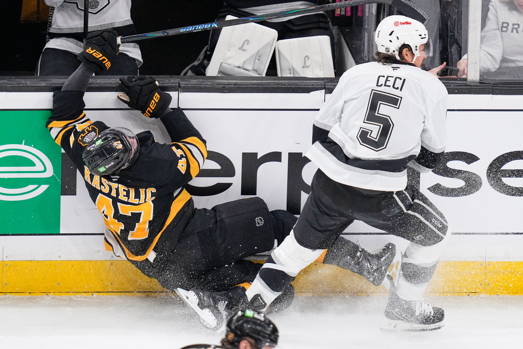 Boston Bruins center Mark Kastelic (47) is checked into the boards by Los Angeles Kings defenseman Cody Ceci (5) during the first period of an NHL hockey game, Tuesday, March 10, 2026, in Boston. (AP Photo/Charles Krupa)