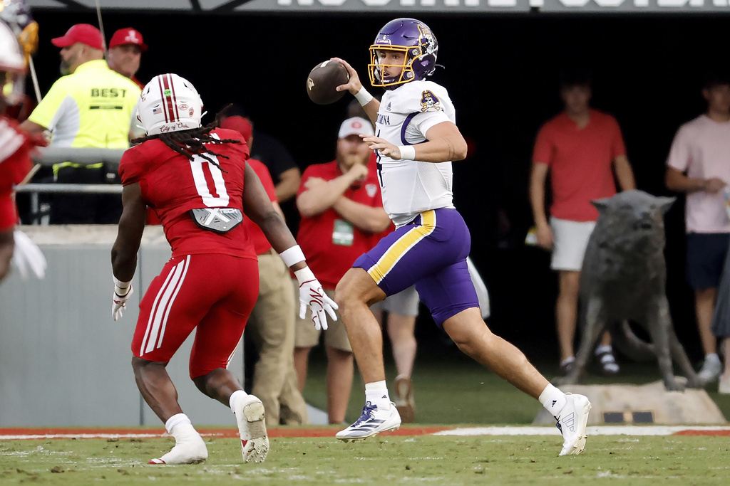 East Carolina's Katin Houser, right,scrambles with the ball away from North Carolina State's Sean Brown (0) during the first half of an NCAA college football game in Raleigh, N.C., Thursday, Aug. 28, 2025. (AP Photo/Karl DeBlaker)