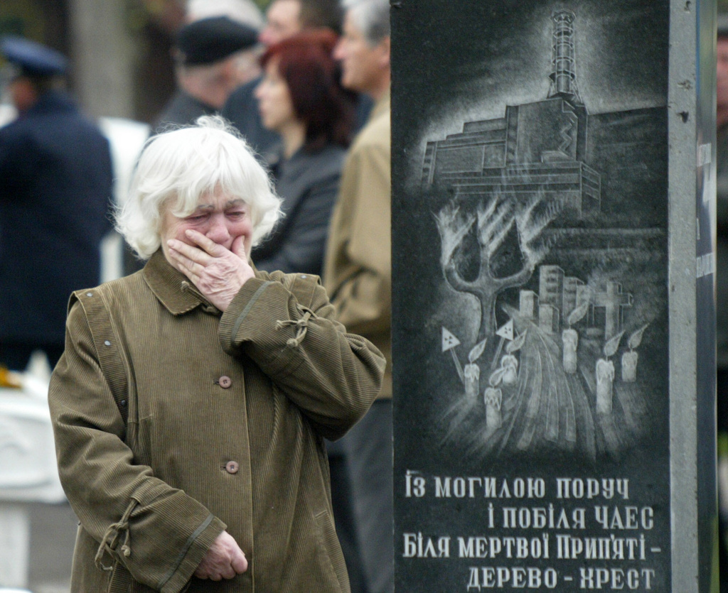 FILE - Alehandra Lihova, sister of a worker who died following cleanup operations from the 1986 explosion and fire at the Chernobyl nuclear power plant, wipes away tears at a wreath-laying ceremony at a monument to victims in Kyiv, Ukraine, April 26, 2004. The monument depicts the plant and its inscription reads "Near the grave, near the Chernobyl nuclear power station, near the dead Prypiat, a tree is the cross." (AP Photo/Efrem Lukatsky, File)
