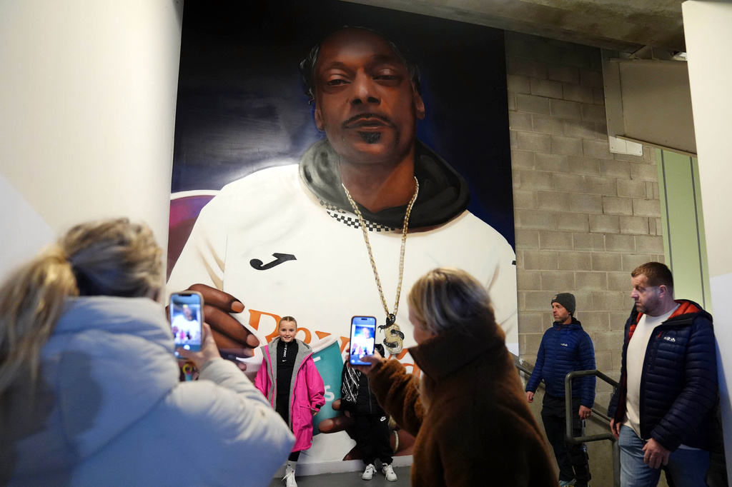 Fans pose for a photograph in front of a mural of Swansea City minority co-owner Snoop Dogg ahead of the English Championship soccer match between Swansea City and Preston in Swansea, Wales, Tuesday, Feb. 24, 2026. (Jacob King/PA via AP)