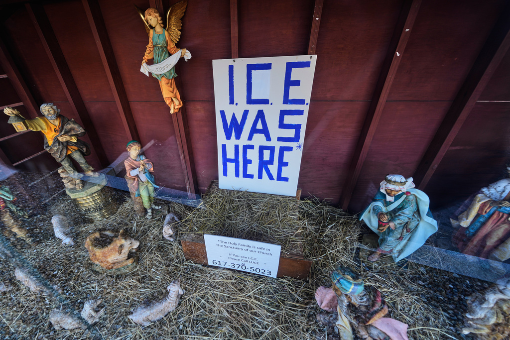 An "ICE WAS HERE" sign is posted in the empty spot for the baby Jesus at a Nativity scene displayed at St. Susanna Church, Tuesday, Dec. 9, 2025, in Dedham, Mass. (AP Photo/Charles Krupa)