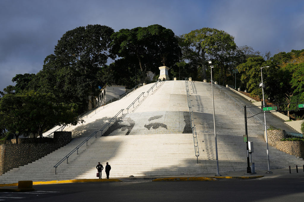 Pedestrians stand in a square decorated with images of the eyes of former President Hugo Chavez in Caracas, Venezuela, Sunday, Jan. 4, 2026. (AP Photo/Ariana Cubillos)