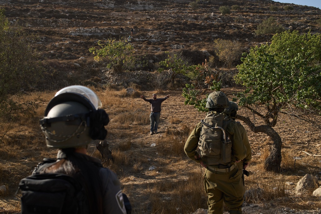 An Israeli settler gestures as Israeli soldiers block access for Palestinians to an area for harvesting olives in the West Bank village of Sa'ir, near Hebron, Thursday, Oct. 23, 2025. (AP Photo/Leo Correa)