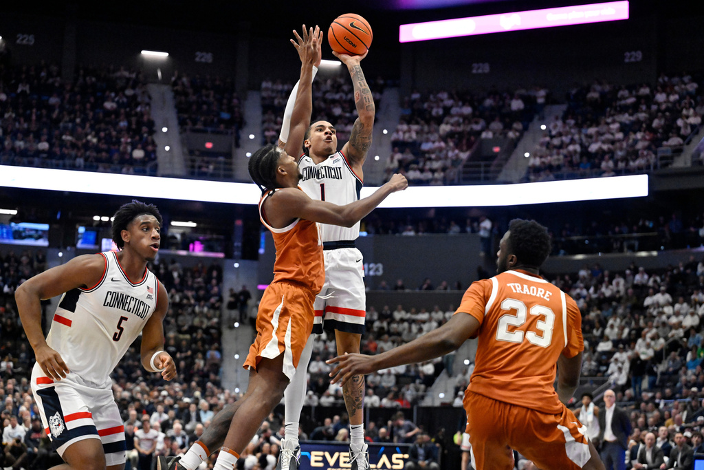 UConn guard Solo Ball (1) shoots over Texas guard Tramon Mark, center left, in the first half of an NCAA college basketball game, Friday, Dec. 12, 2025, in Hartford, Conn. (AP Photo/Jessica Hill)