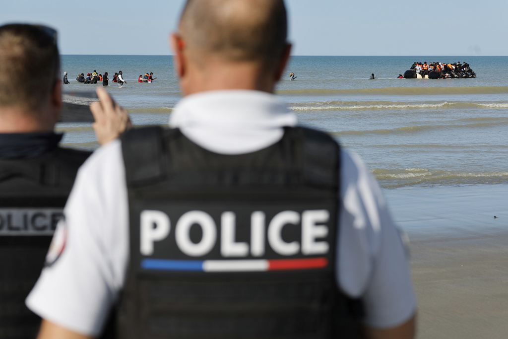 French police officers take photos of migrants as they board a small boat to reach Britain, in Gravelines, northern France, France, Friday, Sept. 19, 2025. (AP Photo/Jean-Francois Badias)
