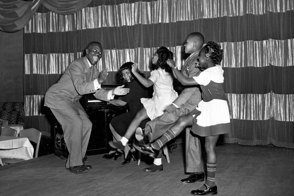 FILE - Tap dancer Bill Robinson, known as Bojangles, far left, is assisted by Mary Bruce on piano as he leads young dancers to the "Charleston Walk" in New York City on Dec. 27, 1944. The children, from left, are, Dorothy Williams, 6; John Whitefield, 8; and Dolgres Jackson, 5. (AP Photo, File)