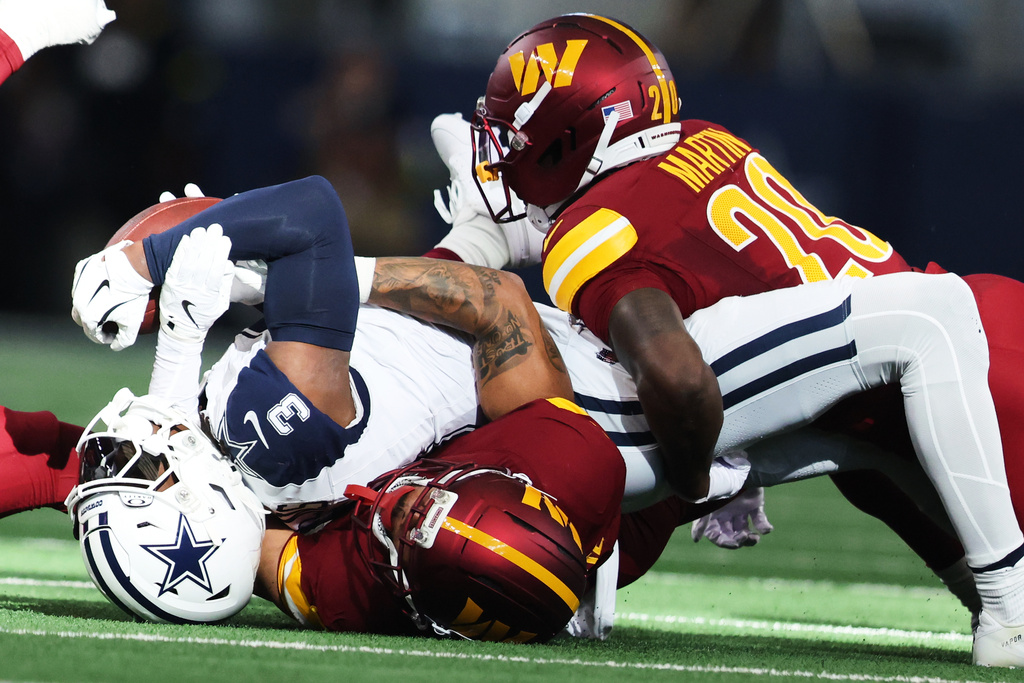 Dallas Cowboys wide receiver George Pickens (3) is tackled by Washington Commanders cornerback Marshon Lattimore, bottom, and safety Quan Martin during the first half of an NFL football game Sunday, Oct. 19, 2025, in Arlington, Texas. (AP Photo/Gareth Patterson)