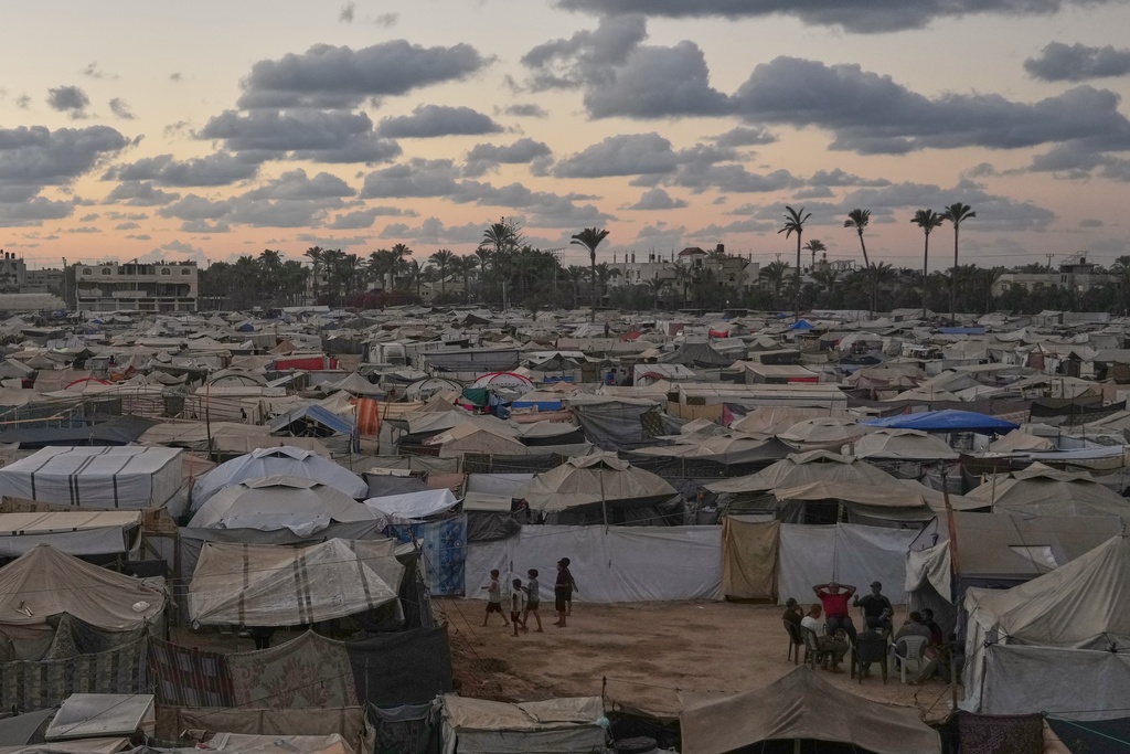 Dusk falls as a group of Palestinians sit outside a tent at a temporary camp in Deir al-Balah, in the central Gaza Strip, Monday, Oct. 6, 2025. (AP Photo/Abdel Kareem Hana)