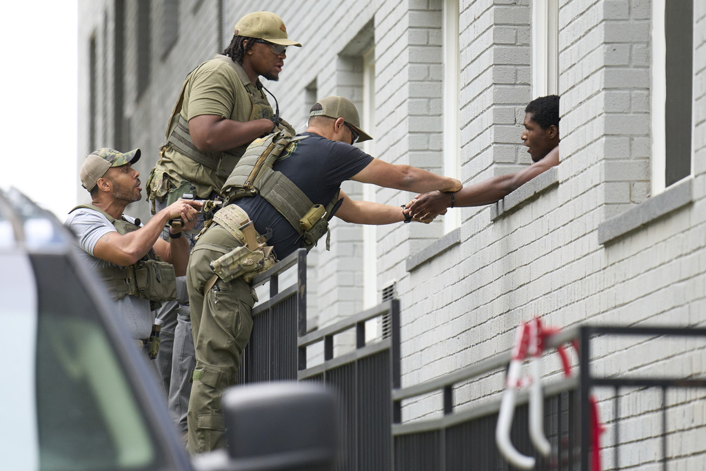Armed Officers place handcuffs on a man from within an apartment complex, Tuesday, Aug. 19, 2025, in the Petworth neighborhood of northwest Washington. The officers pictured had "Washington Field Office" on their shirts underneath tactical gear that said Police. (AP Photo/Jacquelyn Martin)