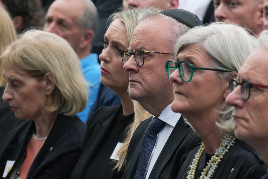 Australia's Prime Minister Anthony Albanese, center right, his wife Jodie Haydon, center left, and other guests participate in a ceremony to mark the National Day of Reflection for victims and survivors, at Bondi Beach in Sydney, Sunday, Dec. 21, 2025, following the Bondi shooting on Dec. 14. (AP Photo/Mark Baker)