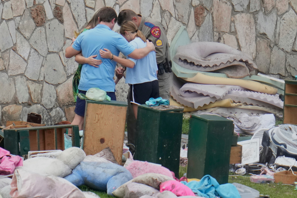 FILE - An officer prays with a family as they pick up items at Camp Mystic in Hunt, Texas on July 9, 2025. (AP Photo/Ashley Landis, file)