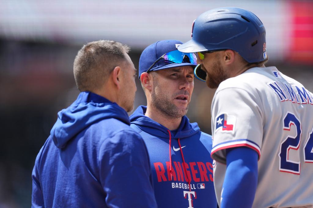 Texas Rangers' Brandon Nimmo, right, confers with manager Skip Schumaker, center, and a trainer before leaving the field after legging out a single in the fifth inning of a baseball game agaisnt the Colorado Rockies, Wednesday, May 20, 2026, in Denver. (AP Photo/David Zalubowski)