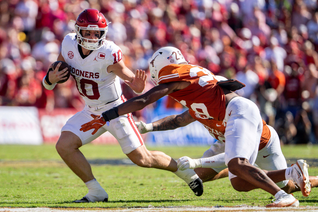 Oklahoma quarterback John Mateer, left, tries to avoid a tackle by Texas linebacker Ty'Anthony Smith (26) as he scrambles during the first half of an NCAA college football game Saturday, Oct. 11, 2025, in Dallas. (AP Photo/Jeffrey McWhorter)