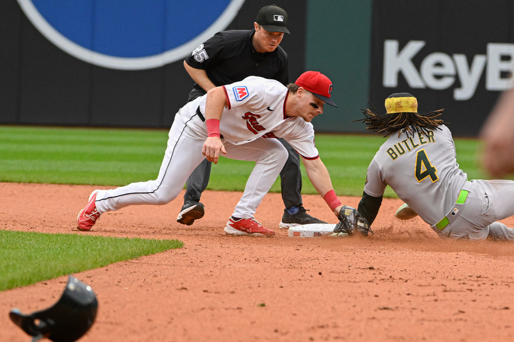Cleveland Guardians' Travis Bazzana, front left, tags out Athletics' Lawrence Butler (4) on a steal-attempt as umpire Junior Valentine, back left, watches during the seventh inning of a baseball game, Sunday, Sept. 20, 2026, in Cleveland. (AP Photo/Phil Long)