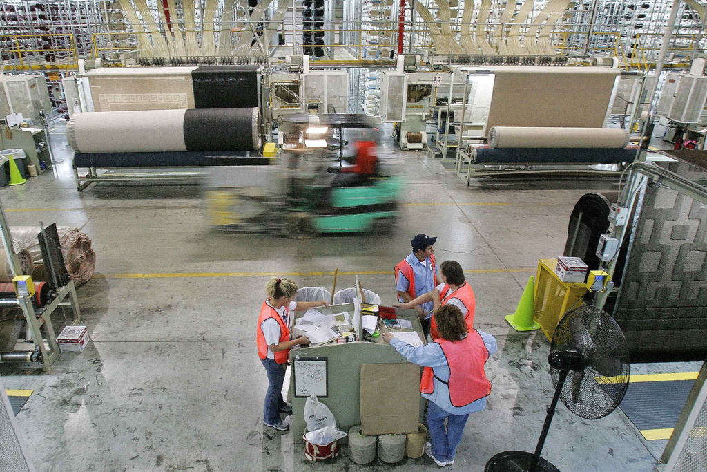 FILE - A forklift speeds by machines and workers on the production floor of a Mohawk Industries rug manufacturing plant in Calhoun, Ga., Wednesday, April 12, 2006. (AP Photo/Ric Feld, File)