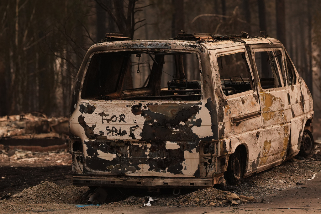 A "for sale" sign is still seen on the back of a van burned after a wildfire hit the northern part of Spokane, Wash., Monday, Aug. 3, 2026. (AP Photo/Lindsey Wasson)