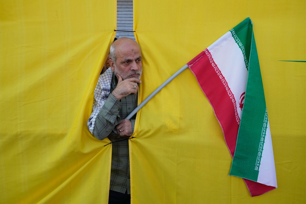 A man holding an Iranian flag peers through an opening in a curtain during the state-organized “Janfada,” or “Sacrifice for Iran,” military-style parade in Tehran, Iran, Friday, Sept. 18, 2026. (AP Photo/Vahid Salemi)