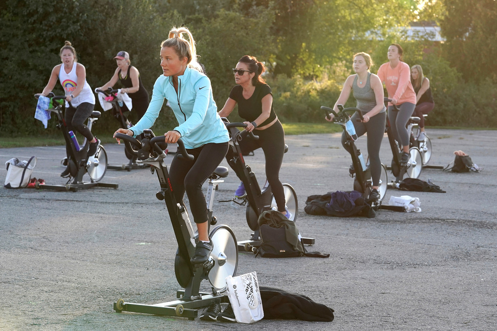 FILE - Jackie Brennan, of Merrimac, Mass., front, pedals on a stationary exercise bike with others during a spinning class in a parking lot outside Fuel Training Studio,Sept. 21, 2020, in Newburyport. (AP Photo/Steven Senne, File)