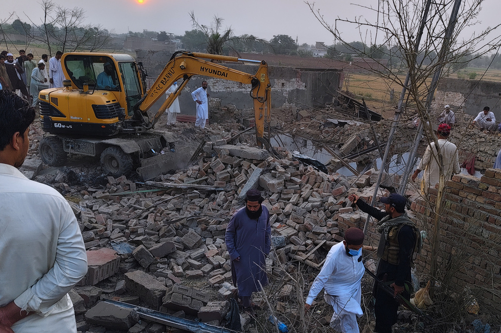 A worker clear rubble with an excavator as a police officer and local residents gather at the site of overnight suicide bombing at a security post in Fatah Khel, in Bannu, a district in Pakistan's Khyber Pakhtunkhwa province bordering Afghanistan, Sunday, May 10, 2026. (AP Photo/Aamad Khattak)
