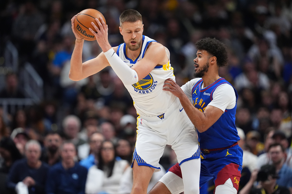Golden State Warriors forward Kristaps Porziņģis, left, fields a pass as Denver Nuggets forward Cameron Johnson defends in the first half of an NBA basketball game Sunday, March 29, 2026, in Denver. (AP Photo/David Zalubowski)