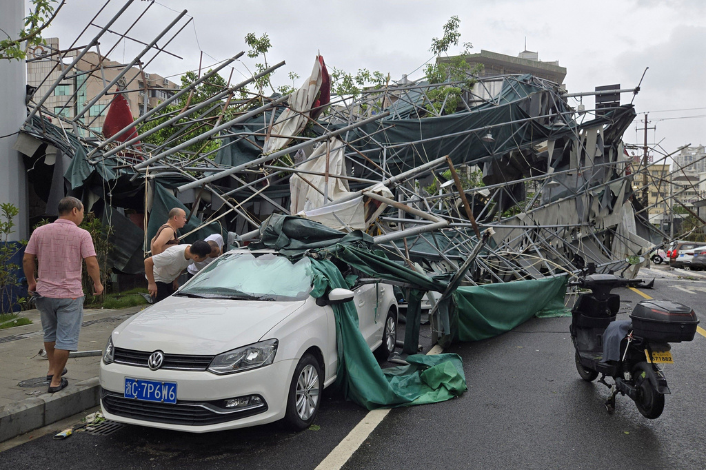 People look inside a car pinned by a fallen scaffolding structure after Typhoon Dolphin affected the area, in Wenzhou in eastern China's Zhejiang province, Monday, Aug. 10, 2026. (Chinatopix Via AP)