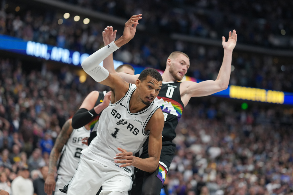 San Antonio Spurs center Victor Wembanyama, front, pursues a loose ball with Denver Nuggets guard Christian Braun in the second half of an NBA basketball game Saturday, April 4, 2026, in Denver. (AP Photo/David Zalubowski)