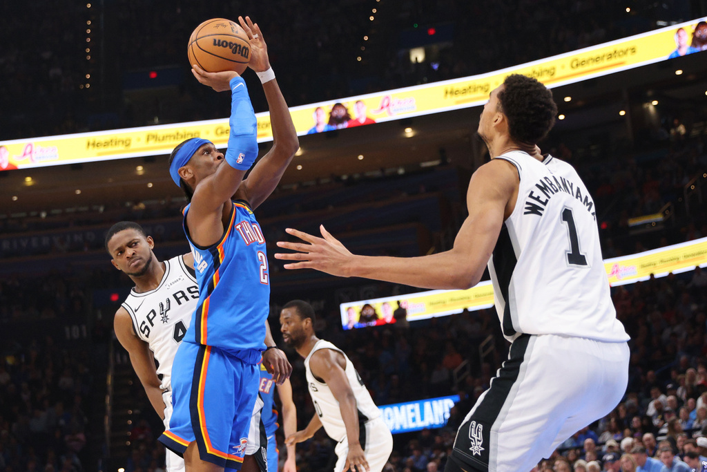 Oklahoma City Thunder guard Shai Gilgeous-Alexander (2) looks to shoot between San Antonio Spurs guard De'aaron Fox, left, and forward Victor Wembanyama (1) during the second half of an NBA basketball game Tuesday, Jan. 13, 2026, in Oklahoma City. (AP Photo/Nate Billings)