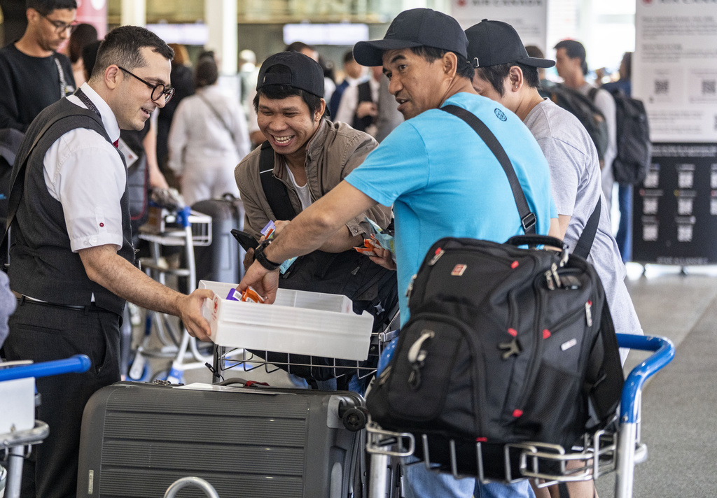 An Air Canada employee hands out snacks to travellers waiting for a flight at Montreal-Pierre Elliott Trudeau International Airport in Dorval, Que., on Tuesday, Aug. 19, 2025. (Christinne Muschi/The Canadian Press via AP)