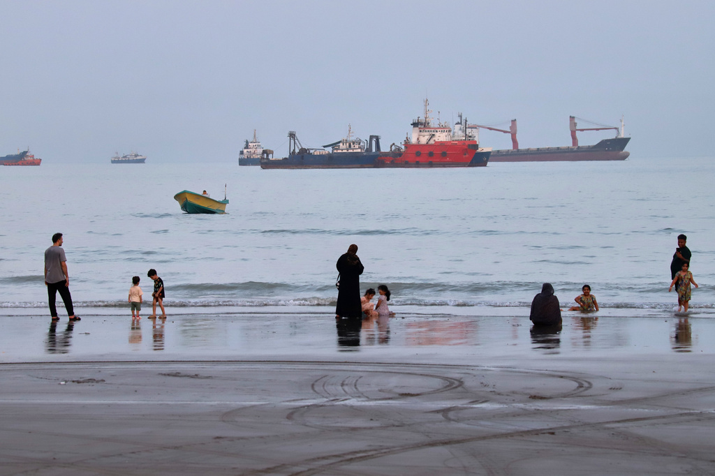 People spend time at a beach as commercial vessels are anchored in the Strait of Hormuz off Bandar Abbas, Iran, Wednesday, Aug. 5, 2026. (Amirhosein Khorgooi/ISNA via AP)