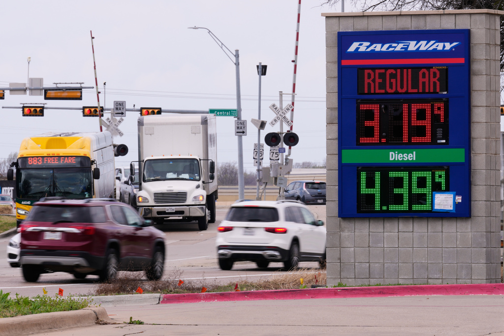 FILE - Drivers navigate a busy intersection past a sign displaying the current gas prices at a filling station in Plano, Texas, March 6, 2026. (AP Photo/Tony Gutierrez, File)