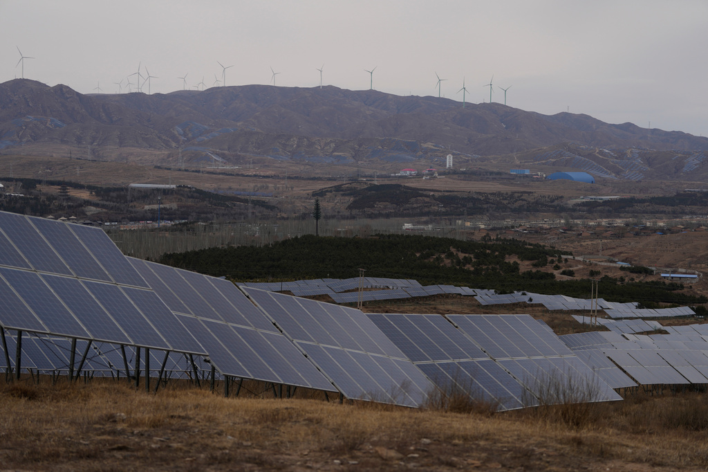 A solar farm operates with wind turbines in the background in Datong, China, Friday, March 13, 2026. (AP Photo/Ng Han Guan)