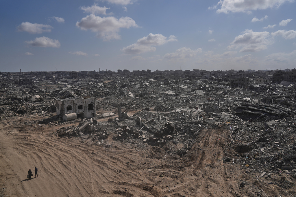 Two displaced Palestinians walk past destroyed buildings in the heavily damaged Sheikh Radwan neighborhood in Gaza City, Saturday, Oct. 11, 2025, after Israel and Hamas agreed to a pause in their war and the release of the remaining hostages. (AP Photo/Abdel Kareem Hana)