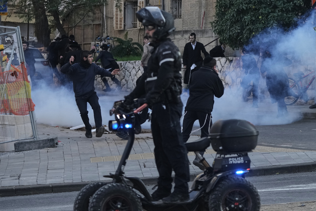 Ultra-Orthodox Jewish protesters run for cover from a gas grenade thrown by Israeli police during a violent disturbance in Jerusalem, Thursday, Dec. 18, 2025. (AP Photo/Mahmoud Illean)