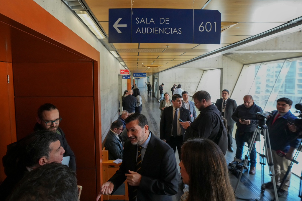 Chief Prosecutor Hector Barros, left center front, talks with members of his legal team outside a hearing room in Santiago, Chile, Friday, Aug. 28, 2026, as they await the arraignment of suspected Tren de Aragua members Rafael Enrique Gámez Salas, known as “El Turko,” and Alfredo Camilo Carrillo Ortiz, known as “El Gocho,” who were extradited from the U.S. and Colombia. (AP Photo/Esteban Felix)