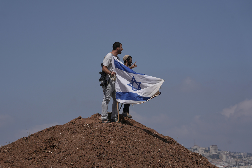 Israeli settlers put up an Israeli flag on a hilltop after it was taken down by Israeli and foreign peace activists during a protest in support of local landowners whose property is threatened with seizure by settlers, on the outskirts of the West Bank city of Beit Sahour, Friday, Aug. 14, 2026. (AP Photo/Mahmoud Illean)