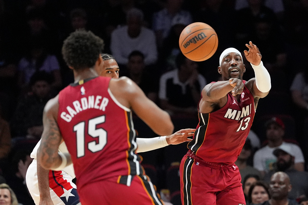 Miami Heat center Bam Adebayo (13) passes to forward Myron Gardner (15) as Washington Wizards center Alex Sarr looks on during the first half of an NBA basketball game, Tuesday, March 10, 2026, in Miami. (AP Photo/Rebecca Blackwell)