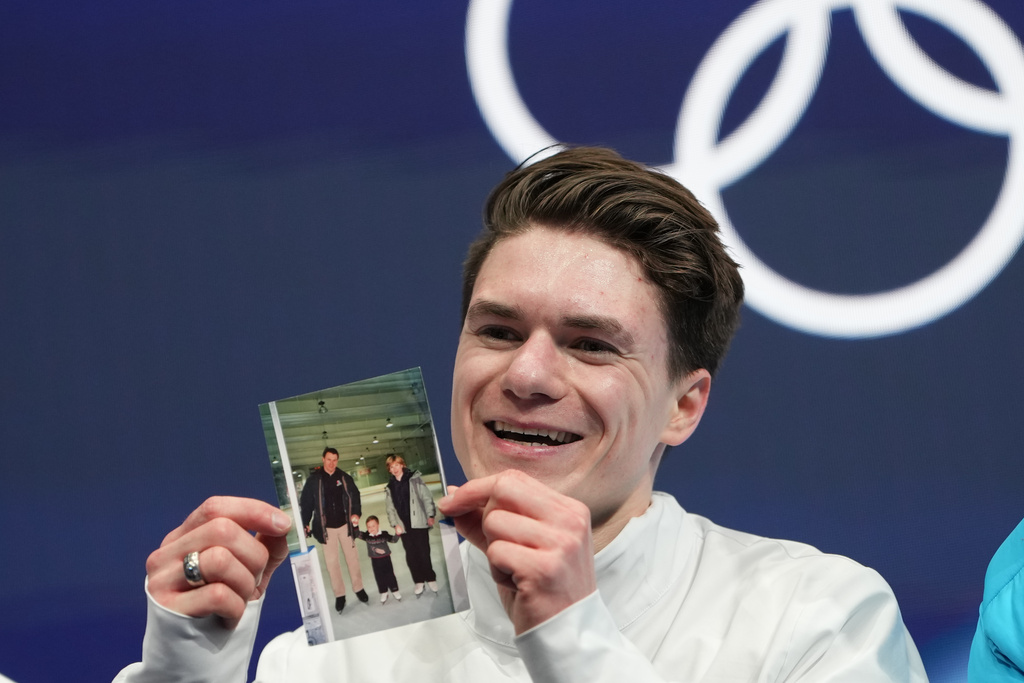 Maxim Naumov of the United States waits for his scores while holding a photo of his parents after competing during the men's figure skating short program at the 2026 Winter Olympics, in Milan, Italy, Tuesday, Feb. 10, 2026. (AP Photo/Francisco Seco)