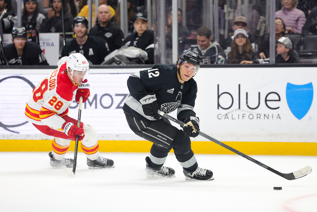 Los Angeles Kings left wing Trevor Moore, right, moves the puck past Calgary Flames defenseman Zach Whitecloud during the second period of an NHL hockey game Saturday, Feb. 28, 2026 in Los Angeles. (AP Photo/Ryan Sun)