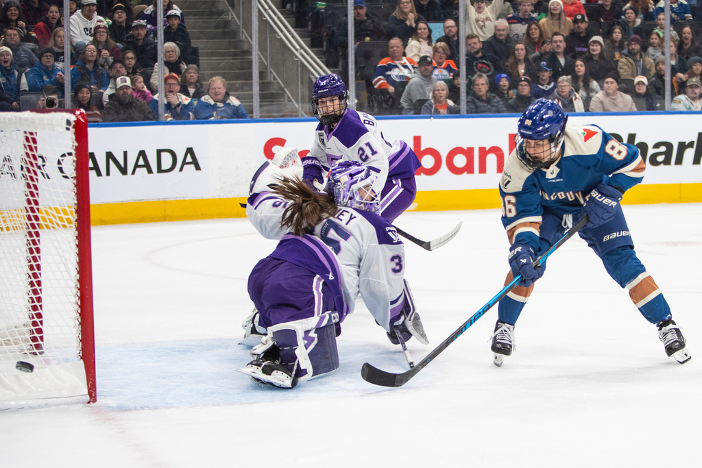 CORRECTS TO PWHL IN EDMONTON, SATURDAY NOT IIHF IN MINNEAPOLIS, FRIDAY - Minnesota Frost goalie Maddie Rooney (35) makes a save against Vancouver Goldeneyes' Michela Cava (86) as Frost's Mae Batherson (21) looks on during second-period PWHL hockey game action in Edmonton, Alberta, Saturday, Dec. 27, 2025. (Amber Bracken/The Canadian Press via AP)