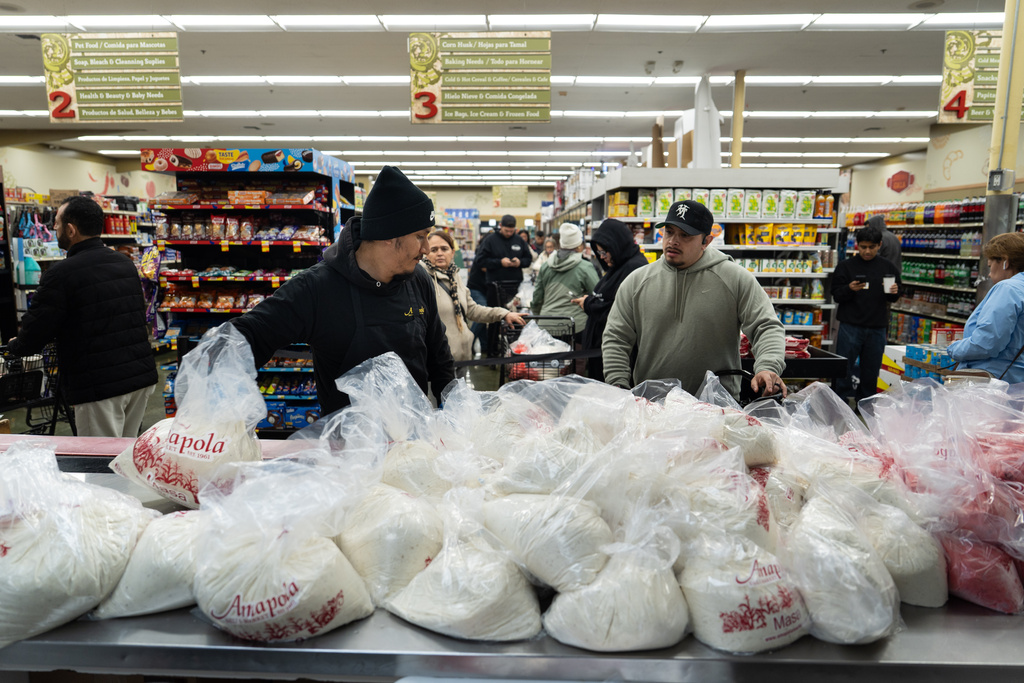 Alex Diaz, left, reaches for a bag of masa, a dough used to make tamales, as shoppers wait in line at Amapola Market in Downey, Calif., Tuesday, Dec. 23, 2025. (AP Photo/Jae C. Hong)