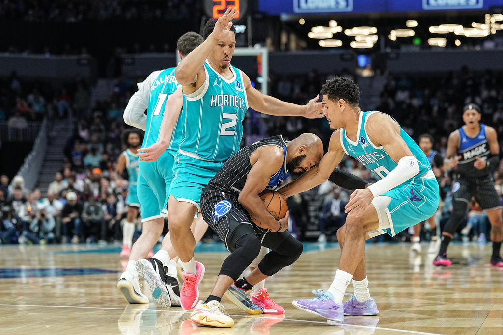 Orlando Magic guard Jevon Carter, center, battles for the ball with Charlotte Hornets forward Grant Williams, left, and guard Josh Green, right, during the first half of an NBA basketball game, Thursday, March 19, 2026, in Charlotte, N.C. (AP Photo/Matt Kelley)