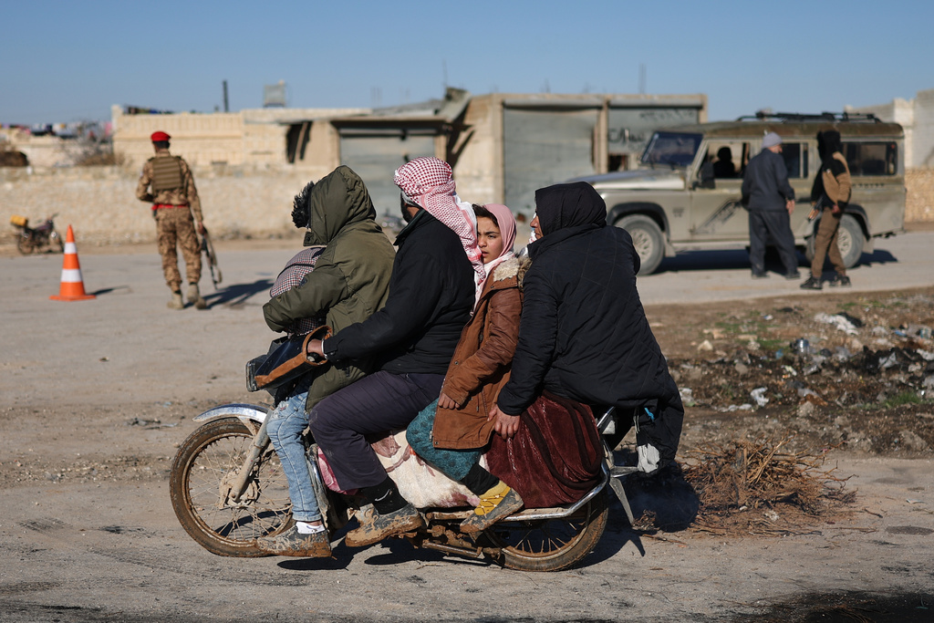 FILE - A displaced Syrian family ride on a motorcycle near the humanitarian crossing declared by the Syrian army in the village of Hamima, in the eastern Aleppo countryside, near the front line with the Kurdish-led Syrian Democratic Forces, in Deir Hafer, Syria, Thursday, Jan. 15, 2026. (AP Photo/Ghaith Alsayed)