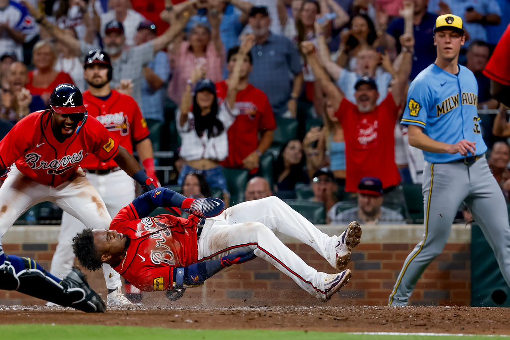 Atlanta Braves second baseman Ozzie Albies, center, scores a run as Milwaukee Brewers pitcher Jacob Misiorowski, right, and Braves' Jorge Mateo, left, look on during the sixth inning of a baseball game, Friday, June 19, 2026, in Atlanta. (AP Photo/Erik S. Lesser)