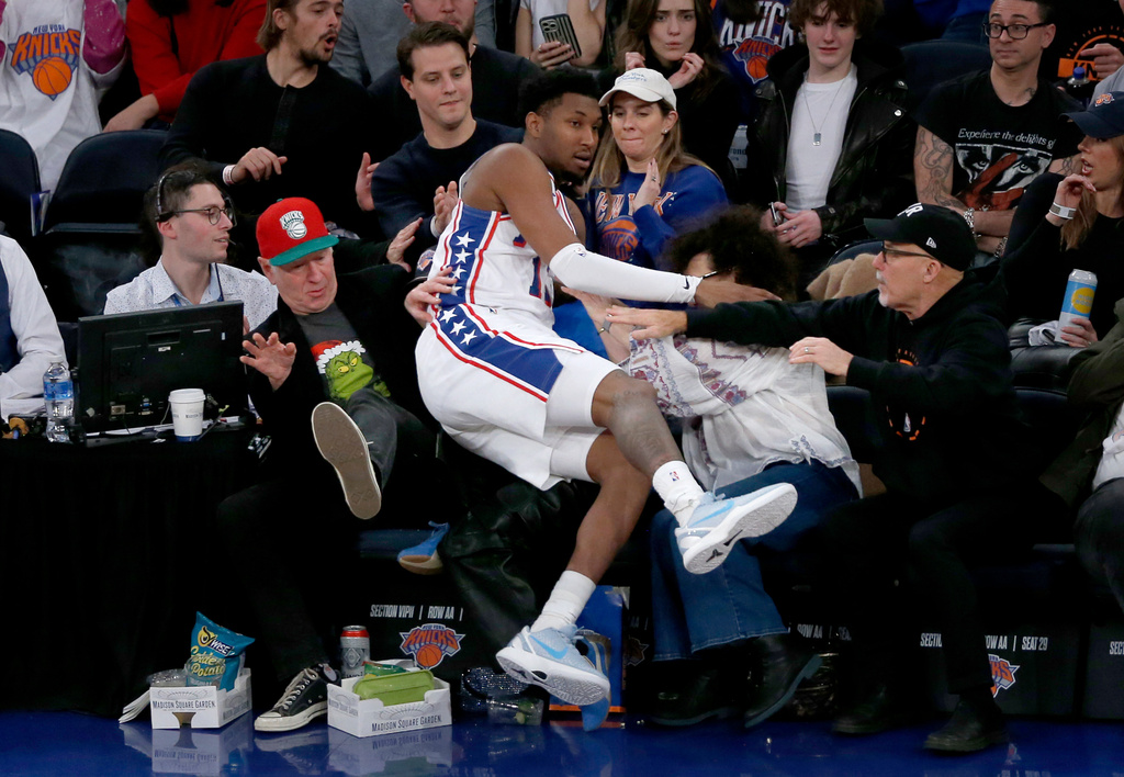 Philadelphia 76ers forward Justin Edwards falls into the lap of former tennis player John McEnroe, left, in red hat, during the first half of an NBA basketball game against the New York Knicks, Friday, Dec. 19, 2025, in New York. (AP Photo/John Munson)